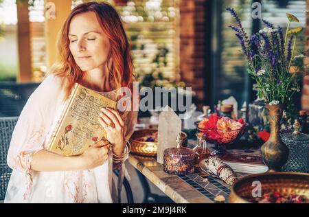 La femme tient un livre ornemental et une anque égyptienne. Table avec fleur de rose et huile essentielle. Spa et aromathérapie. Banque D'Images