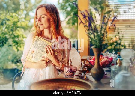 La femme tient un livre ornemental et une anque égyptienne. Table avec fleur de rose et huile essentielle. Spa et aromathérapie. Banque D'Images