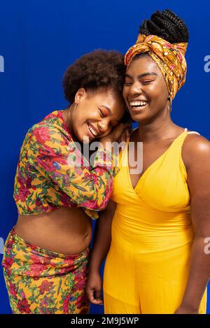 Portrait de deux femmes sur fond bleu. L'un d'eux est enceinte et repose sa tête sur l'épaule des autres. Banque D'Images