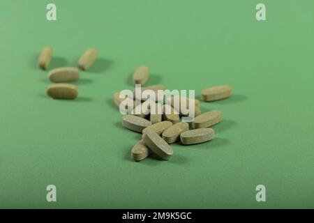 Pilules fines herbes et vitamine Green posées librement sur fond vert Banque D'Images