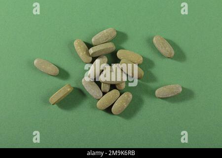 Pilules fines herbes et vitamine Green posées librement sur fond vert Banque D'Images