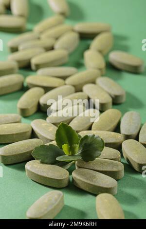 Pilules fines herbes et vitamine Green posées librement sur fond vert Banque D'Images