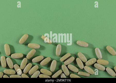 Pilules fines herbes et vitamine Green posées librement sur fond vert Banque D'Images