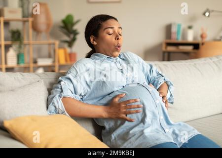 Femme enceinte afro-américaine touchant le ventre, souffrant de contractions douloureuses et faisant des exercices de respiration Banque D'Images