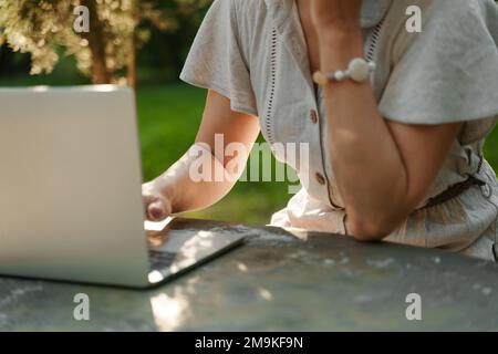 une belle femme mature en chapeau travaille sur un ordinateur à une table blanche dans la nature et passe sa journée productive Banque D'Images