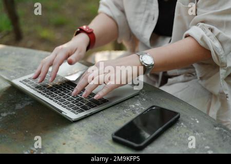 une belle femme mature en chapeau travaille sur un ordinateur à une table blanche dans la nature et passe sa journée productive Banque D'Images