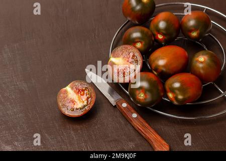 Tomates rouges foncé sur un gril en métal. Deux moitiés d'une tomate rouge et d'un couteau. Copier l'espace. Vue de dessus. Arrière-plan marron. Banque D'Images