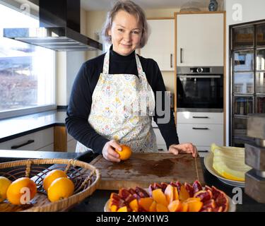 Une femme d'âge moyen dans un tablier de cuisine prépare une tranche de fruits brillants Banque D'Images