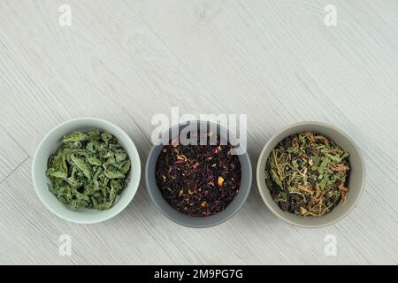 Variété de tisanes dans des bols sur fond de bois clair. Ensemble de feuilles aromatiques. Pose à plat. Banque D'Images