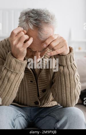 homme âgé avec syndrome parkinsonien et mains tremblantes assis avec la tête courbée à la maison, image de stock Banque D'Images