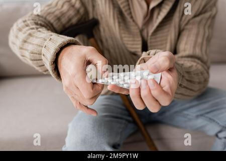 vue partielle d'un homme âgé souffrant du parkinsonisme et tenant des pilules dans les mains tremblantes tout en étant assis à la maison, image de stock Banque D'Images