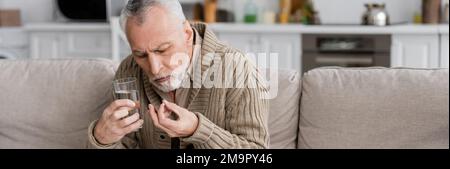 homme senior tenant la pilule et le verre d'eau dans les mains tremblantes tout en souffrant du syndrome de parkinson, bannière, image de stock Banque D'Images