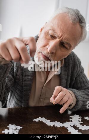 homme à poil gris souffrant du syndrome parkinsonien et tenant un élément de puzzle dans la main tremblante, image de stock Banque D'Images