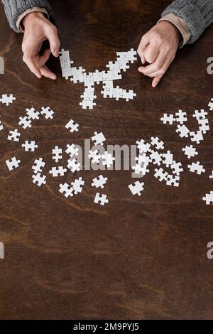 vue de dessus de l'homme de culture avec des mains tremblantes souffrant de la maladie de parkinson et combinant puzzle sur table en bois, image de stock Banque D'Images