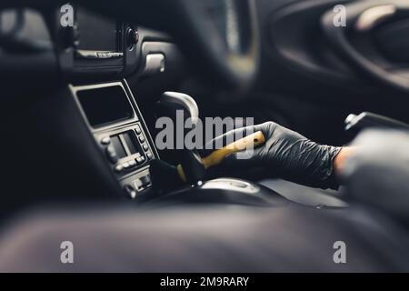 Un homme nettoyant l'intérieur noir de la voiture avec une brosse. Concept de détail de voiture. Gros plan avec un premier plan flou. Photo de haute qualité Banque D'Images