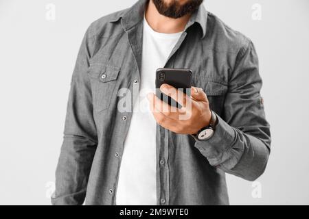 Jeune homme d'affaires utilisant un téléphone portable sur fond clair, gros plan Banque D'Images