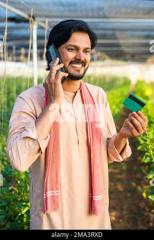 coup de feu vertical de jeunes agriculteurs à la serre parlant sur téléphone mobile en tenant la carte de crédit verte - conept de paiement en ligne, le service à la clientèle et Banque D'Images