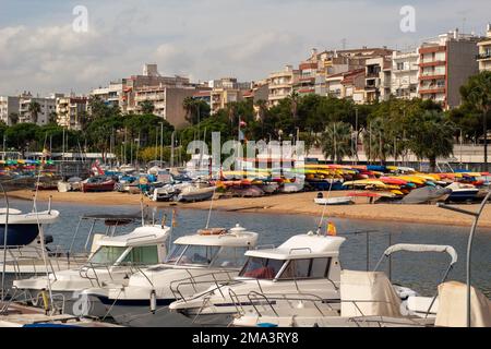 Petit port de pêche du village de Blanes avec les bateaux garés et les bâtiments du village en arrière-plan sous un ciel bleu avec des nuages. Banque D'Images