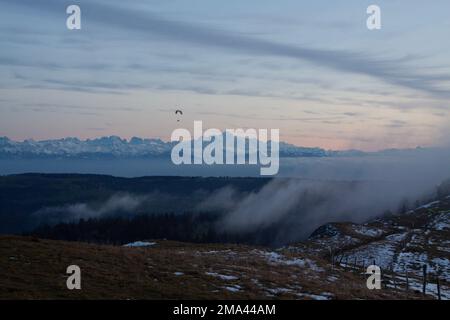 Parapente survolant les montagnes du Jura avec les Alpes enneigées en arrière-plan Banque D'Images