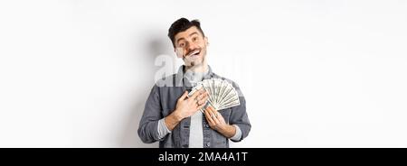 Un homme souriant qui fait de l'argent, enserre des billets de dollars avec un visage soulagé heureux, debout sur fond blanc Banque D'Images