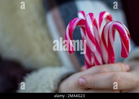 Femme distribuant des cannes de Noël aux enfants dans les rues de Madrid bien enveloppées dans un manteau et une écharpe avec un pull en laine. Banque D'Images