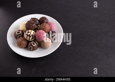 photo de nombreux chocolats de couleur sur une assiette sur fond noir Banque D'Images