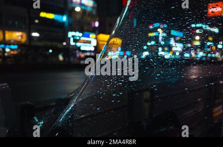 Photo de fond de ville de nuit abstraite, lumières de rue floues et gouttes de pluie sur verre Banque D'Images