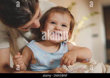 Maman souriante enseignant à sa petite fille brodant avec des aiguilles, se relaxant ensemble à la maison. Engagé dans des activités de loisir le week-end Banque D'Images