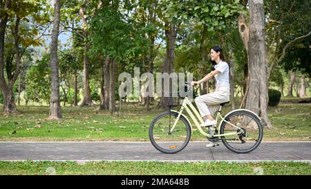 Une jeune femme asiatique décontractée et décontractée vêtue de vêtements confortables à vélo sur la piste cyclable du parc. concept de passe-temps et d'exercice Banque D'Images