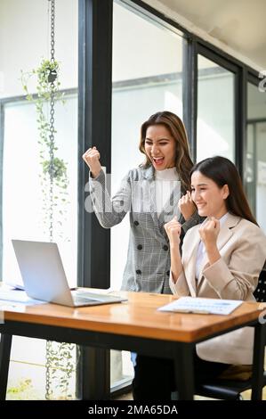 Portrait, deux femmes d'affaires asiatiques du millénaire surjoyeuses et enthousiastes regardant l'écran d'ordinateur portable, recevant de bonnes nouvelles, célébrant leur succès de projet à Banque D'Images