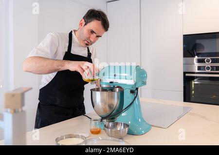 Un boulanger d'homme cuit un gâteau de velours rouge à la maison, en préparant le gâteau en ajoutant de l'huile dans le robot de cuisine, le travail à la maison Banque D'Images