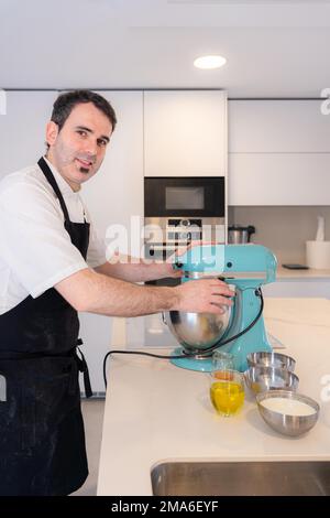 Un boulanger d'homme cuit un gâteau de velours rouge à la maison, préparant le gâteau dans le robot de cuisine, travailler à la maison Banque D'Images