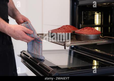 Un boulanger d'homme cuit un gâteau de velours rouge à la maison, en prenant le gâteau cuit hors des casseroles du four Banque D'Images