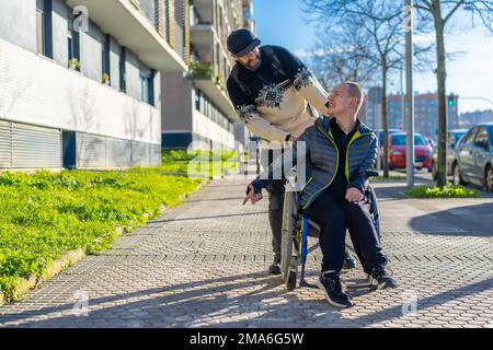 Une personne handicapée en fauteuil roulant marchant avec un ami sur une chaise dans la rue en hiver Banque D'Images