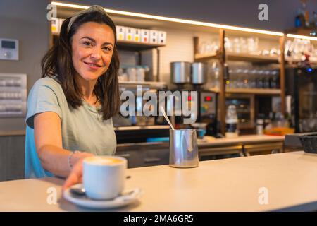 Serveuse souriante à la cafétéria avec le café préparé le donnant au client, les restrictions dues au covid sont supprimées et l'utilisation obligatoire Banque D'Images