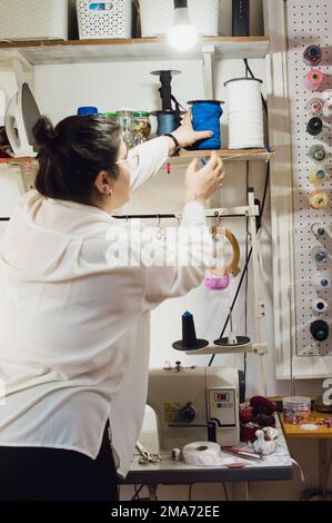 vue arrière d'une jeune entrepreneur debout travaillant dans son atelier de couture maison, image verticale. Banque D'Images