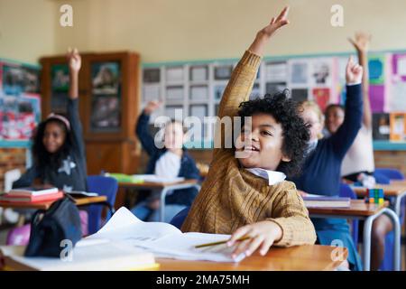 Choisissez-moi, choisissez-moi. un groupe diversifié d'enfants assis dans leur classe scolaire et levant les mains pour répondre à une question. Banque D'Images