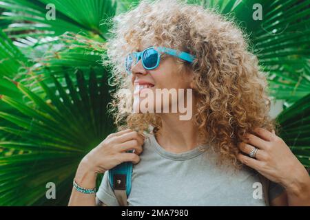 Bonne touriste féminine avec sac à dos Profitez du parc naturel et sourire contre un fond vert de grandes feuilles tropicales. Les gens et les vacances de printemps. loisirs en plein air Banque D'Images