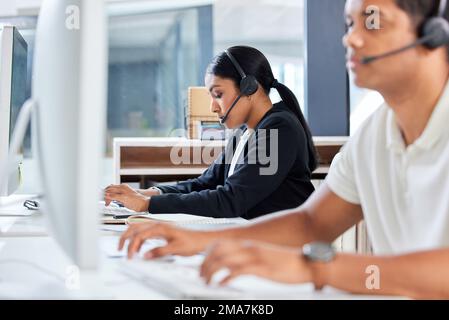 Résolution des problèmes un par un. deux jeunes hommes d'affaires assis au bureau et portant des micro-casques tout en utilisant un ordinateur. Banque D'Images