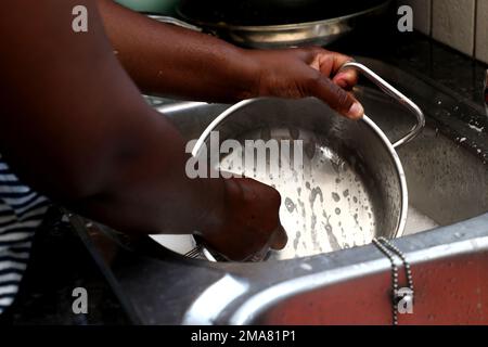 Une femme africaine séchant une casserole avec une serviette de cuisine dans la cuisine Banque D'Images