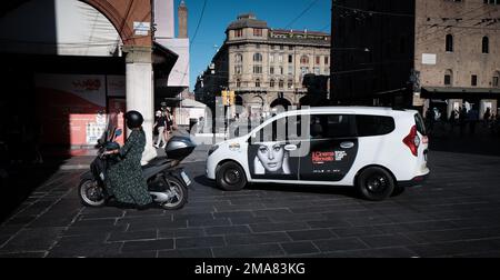 Une motard femme vêtue d'une robe se déplace à côté d'un taxi avec une publicité du cinéma Ritrovato avec une image de Sophie Loren à la porte de Bologne Banque D'Images