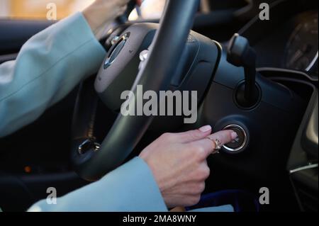 Gros plan du doigt de la femme appuyant sur le bouton de démarrage/arrêt du moteur de la voiture de luxe moderne. Concept de voiture de conduite Banque D'Images