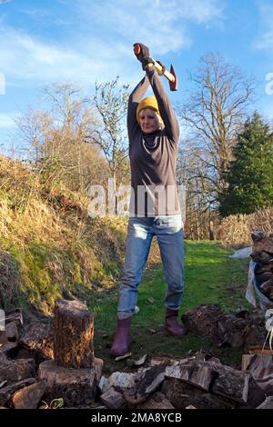 Femme âgée de 75 ans 70s se faire de l'exercice pour garder au chaud des bûches de broyage pour le bois de chauffage avec une hache dans les zones rurales du pays de Galles Royaume-Uni Grande-Bretagne KATHY DEWITT Banque D'Images