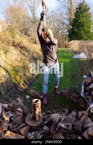 Femme âgée de 75 ans 70s se faire de l'exercice pour garder au chaud des bûches de broyage pour le bois de chauffage avec une hache dans les zones rurales du pays de Galles Royaume-Uni Grande-Bretagne KATHY DEWITT Banque D'Images