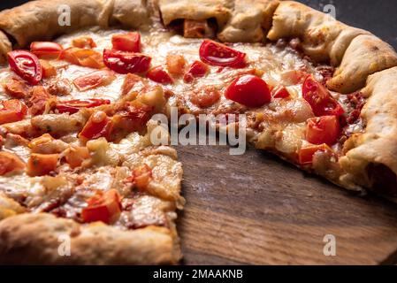 gros plan de savoureuses pizzas en tranches avec tomates et herbes sans une tranche sur fond de table en bois. Banque D'Images