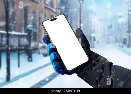 Utiliser un téléphone mobile dans la rue pendant qu'il neige. Affichage isolé pour la promotion des applications. Main de l'homme tenant un téléphone avec un gant d'hiver Banque D'Images