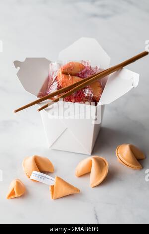 Un récipient de nourriture à emporter rempli de biscuits fortune avec des biscuits devant. Banque D'Images