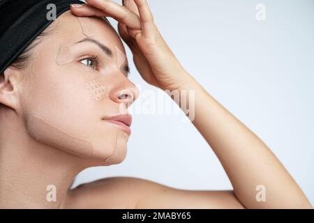 Femme adulte appliquant des bandes kinésio sur son visage, rides du visage tapant. Banque D'Images