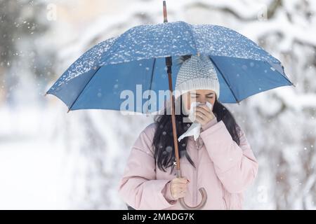 La femme tient un parapluie tout en se défrichant le nez en raison de la grippe hivernale. Banque D'Images