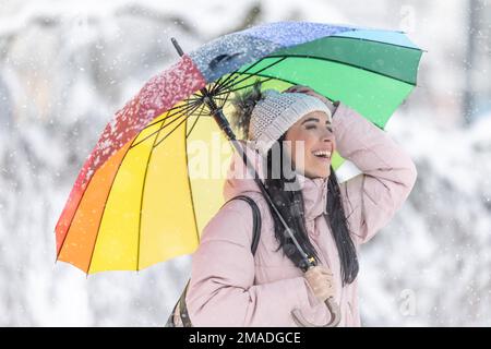 Une femme heureuse sous un parapluie qui apprécie les chutes de neige et les flocons qui tombent. La brunette est heureuse de l'hiver qui vient et de la forte chute de neige. Banque D'Images